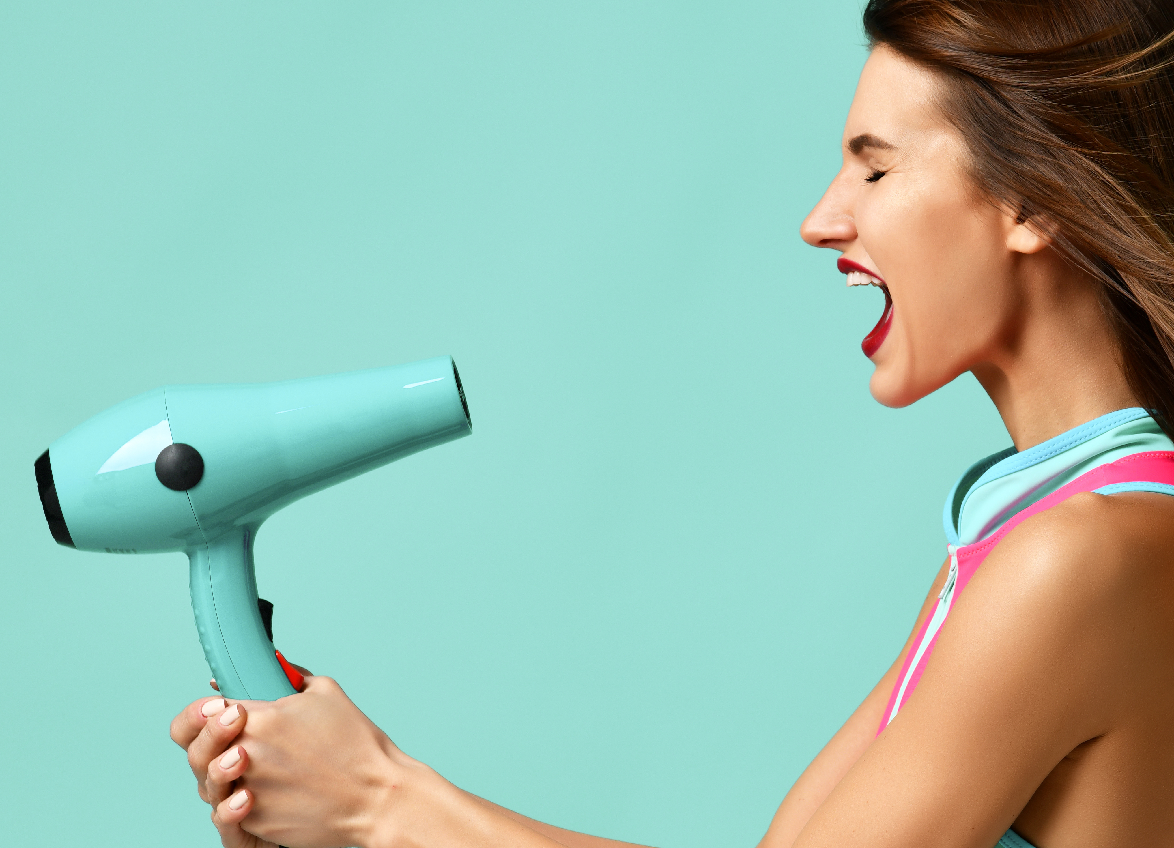 Happy young brunette woman with hair dryer on blue mint background. Hair style beauty concept